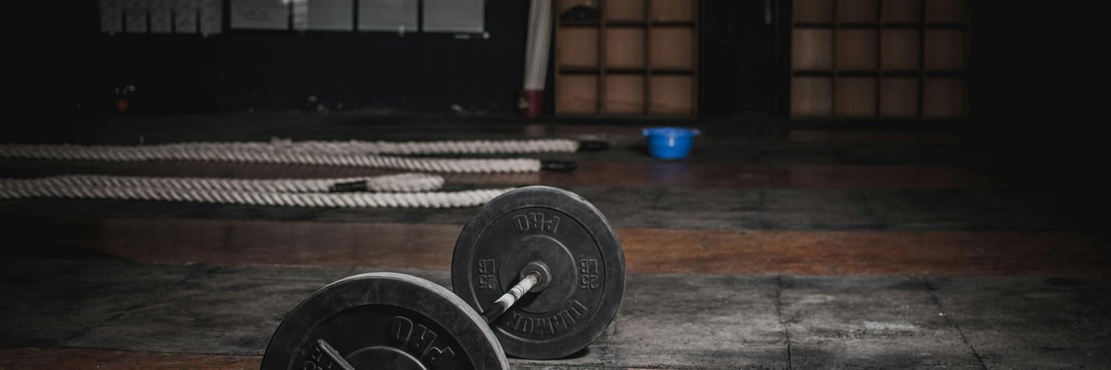 A pair of dumbbells on a gym floor with equipment in the background.